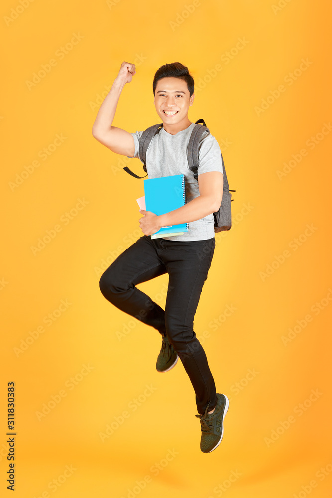 兴奋的亚洲年轻男子背着背包在橙色背景上跳跃
