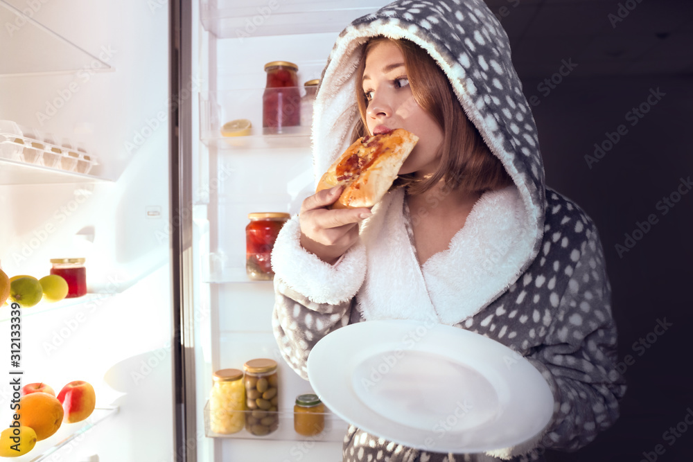 十几岁的女孩晚上在冰箱附近吃不健康的食物