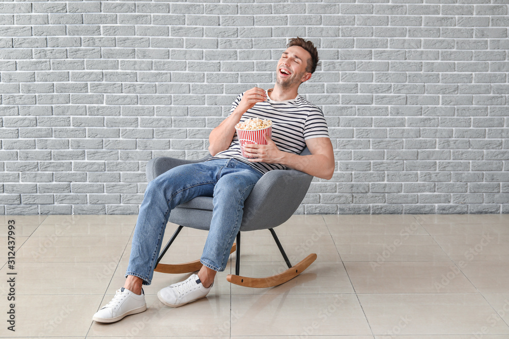 快乐男人坐在灰色墙壁附近的扶手椅上看电影