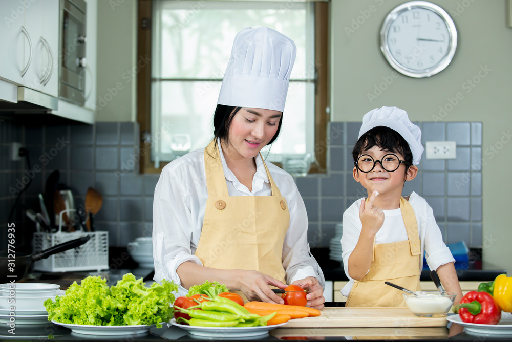快乐的亚洲妈妈和儿子在hom的现代厨房里准备新鲜的蔬菜和水果