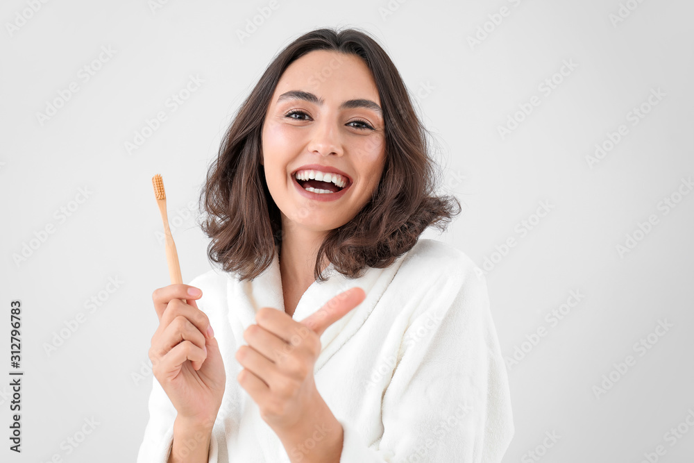 漂亮的年轻女人拿着牙刷，在浅色背景下展示拇指向上的姿势