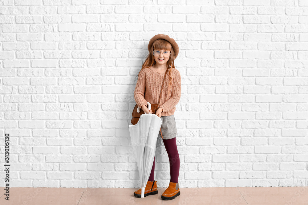Cute fashionable girl with umbrella near white brick wall