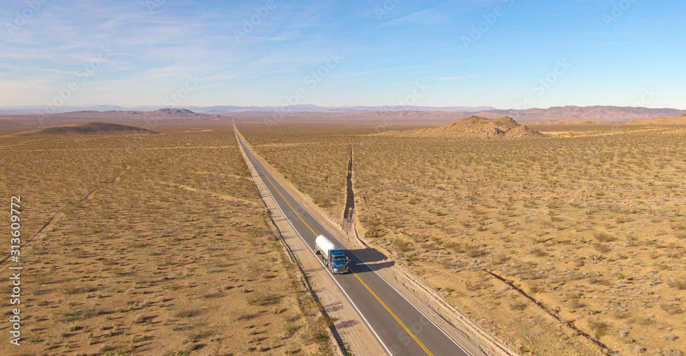 AERIAL: Big rig hauls a cistern across the rugged Mojave desert on a sunny day.