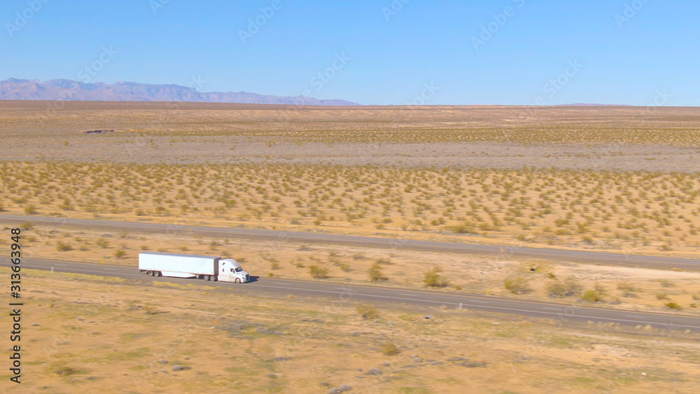 无人机：在犹他州沙漠中长途行驶的白色货运卡车上方飞行。