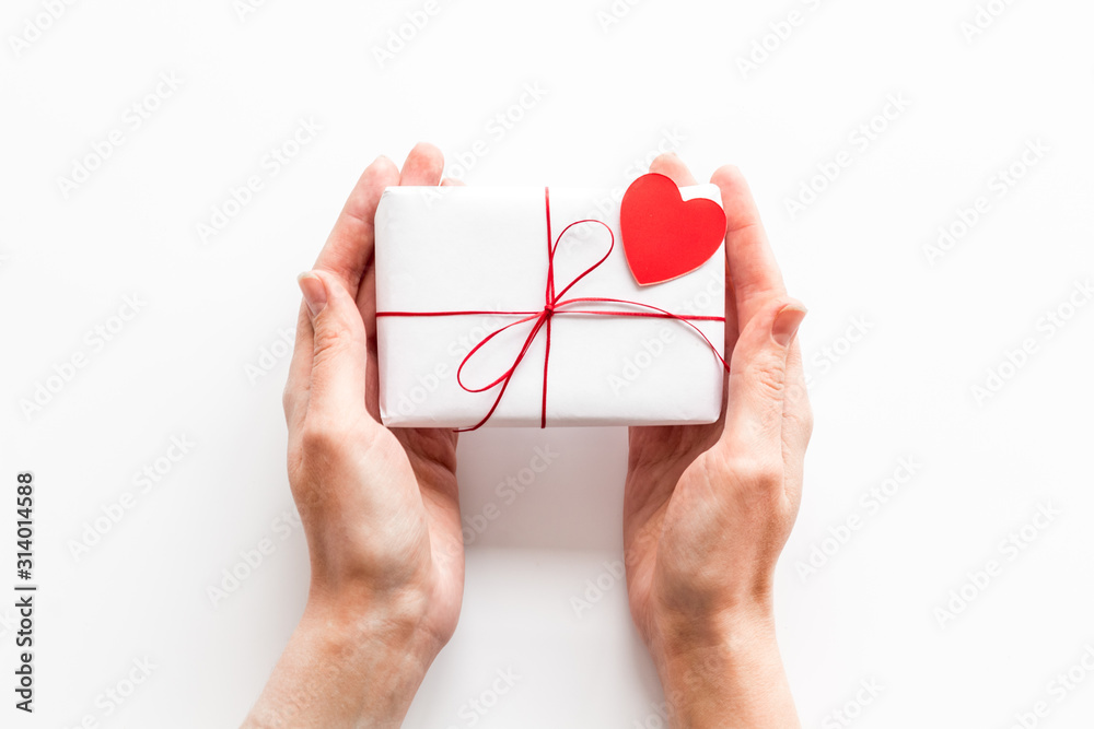 Give a gift on Valentines Day. Women hand hold present box decorated with small heart on white back