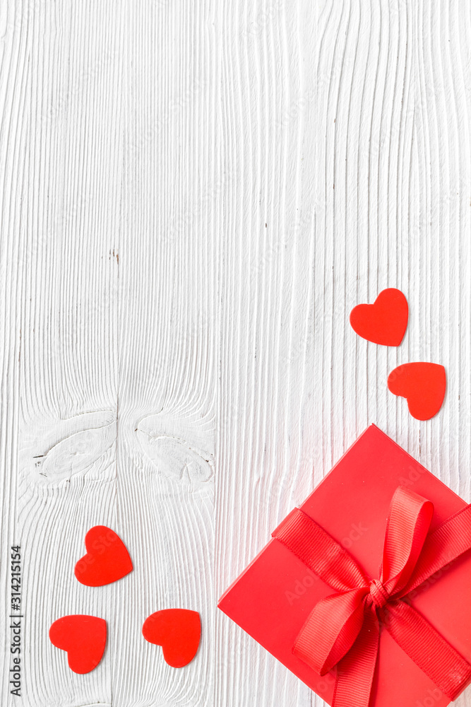 Gift to a sweetheart on Valentines Day. Red present box near hearts on white wooden background top-