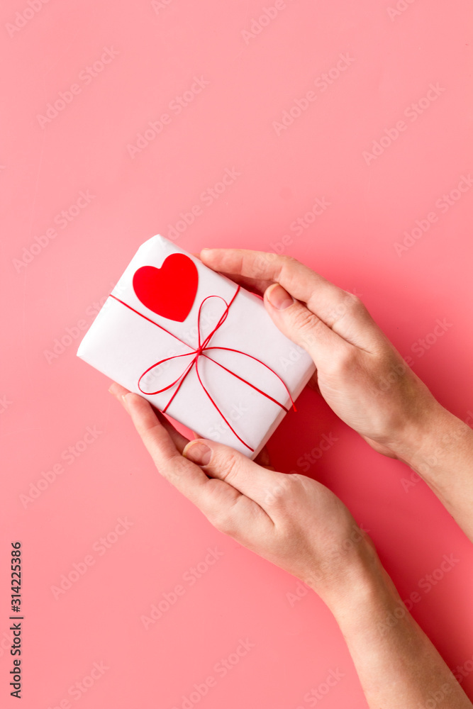 情人节礼物。女性手持礼品盒，粉色背景装饰有小心形t