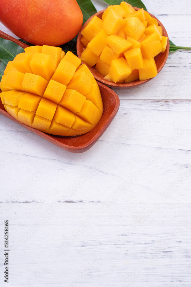 新鲜的芒果，美丽的切碎的水果，明亮的木桌背景上有绿叶。热带水果