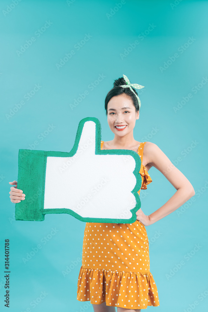 Portrait of charming young woman holding big LIKE icon isolated on blue background in studio. People