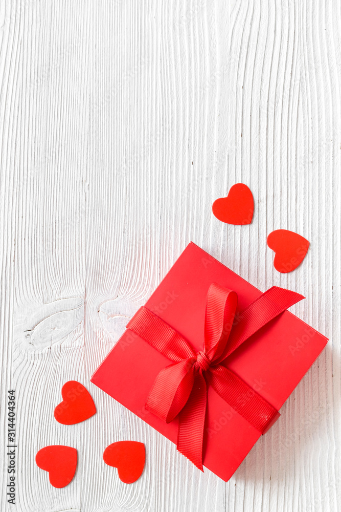 Gift to a sweetheart on Valentines Day. Red present box near hearts on white wooden background top-