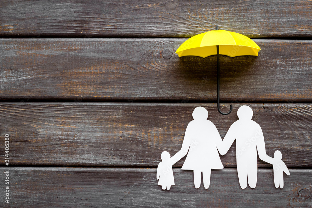 Live insurance concept. Family silhouette protected by umbrella on dark wooden background top-down c