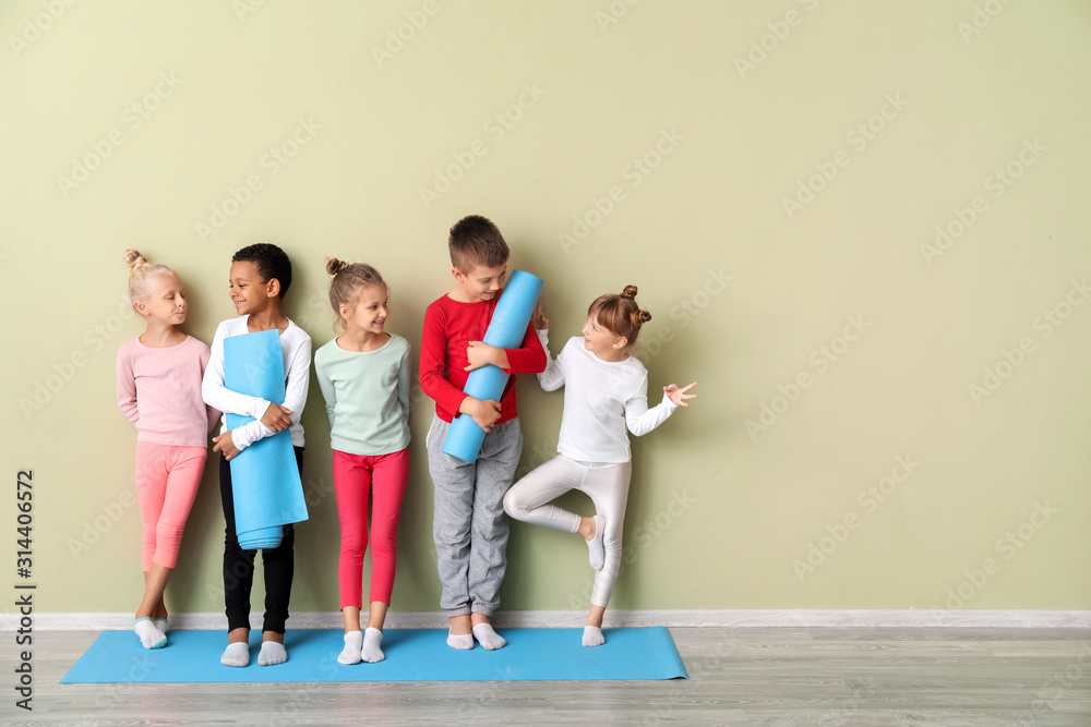 Little children with yoga mats near color wall in gym