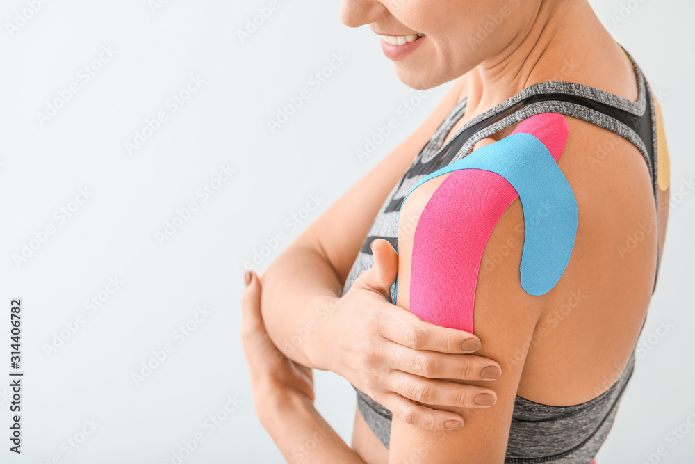 Sporty woman with physio tape applied on shoulder against light background, closeup
