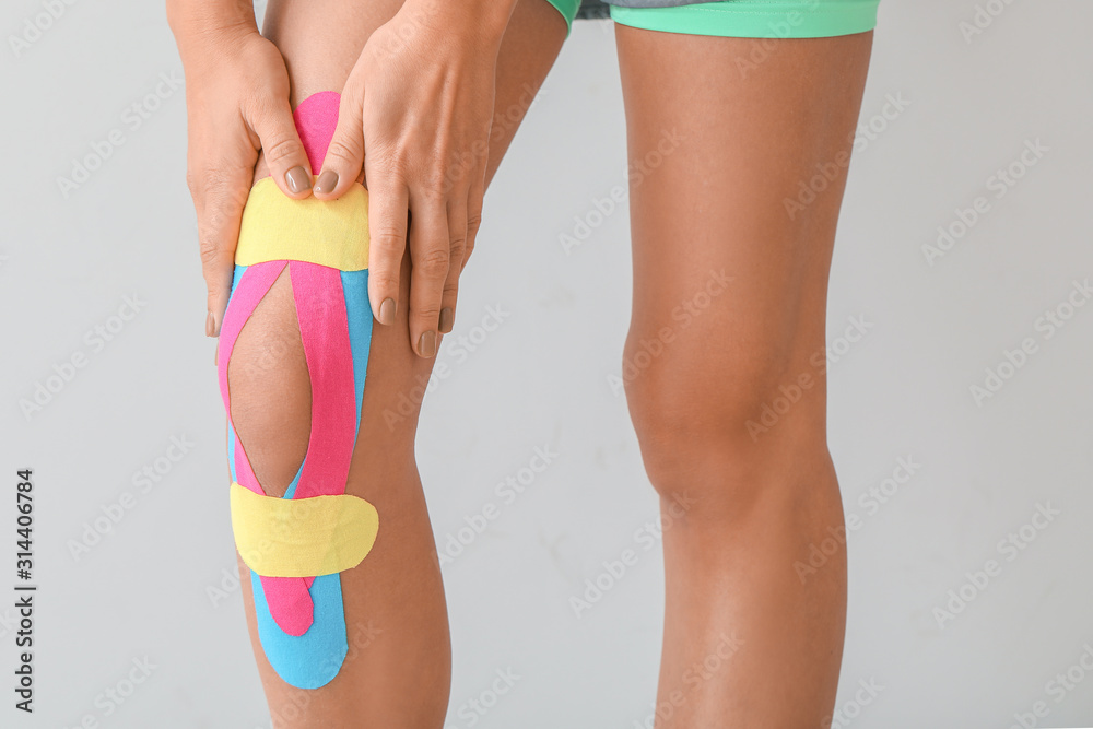 在浅色背景下，膝盖上贴着理疗胶带的运动型女性，特写镜头