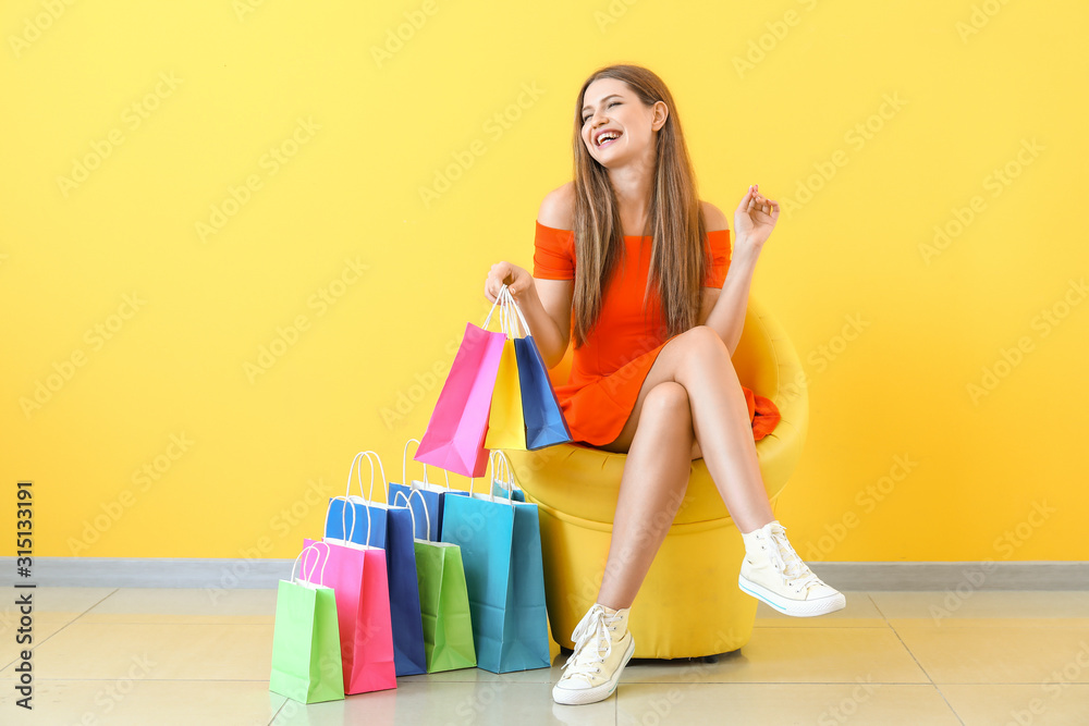 漂亮女人拿着购物袋坐在靠近彩色墙的扶手椅上