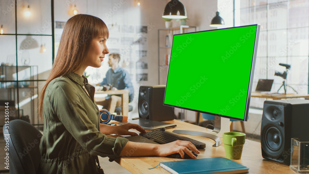 美丽的深色皮肤女性视频编辑在她的个人电脑上用大绿屏幕模型工作
