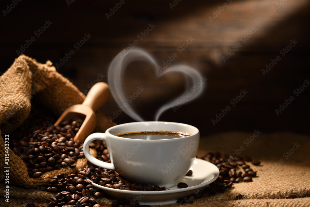 一杯咖啡，带有心形烟雾，咖啡豆放在旧木质背景的麻袋上