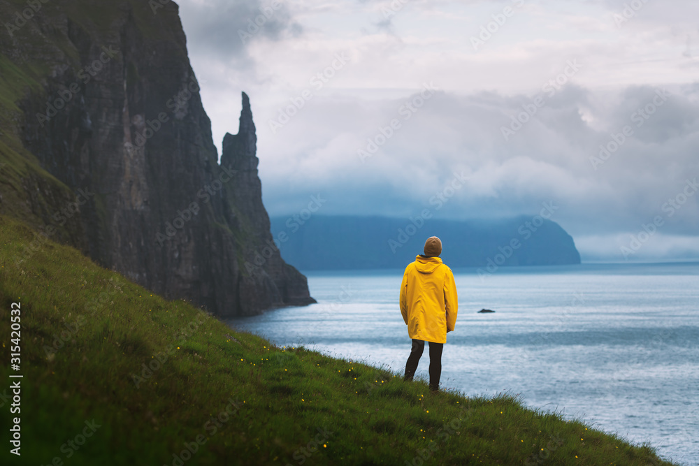 穿着黄色夹克的游客从Trollkonufinger的视角看女巫手指悬崖。Vagar岛