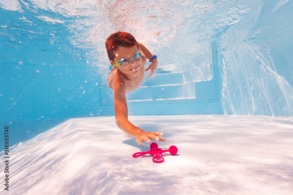小快乐的孩子戴着谷歌在游泳池里潜到水下的玩具