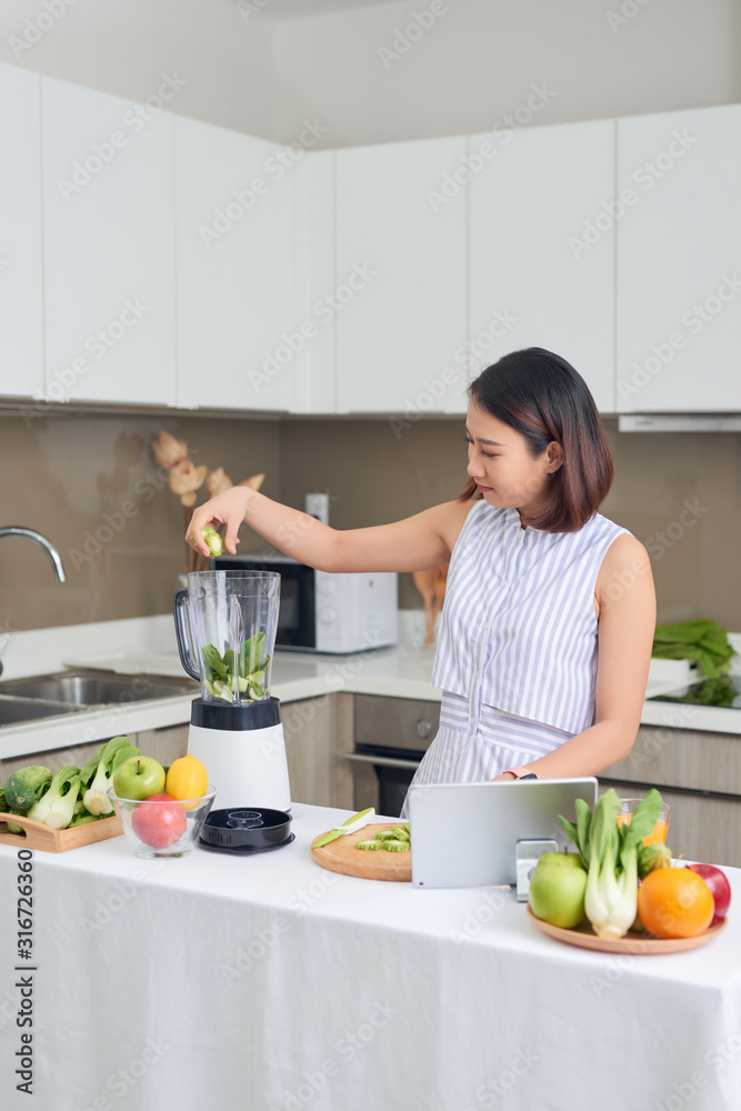 美丽的亚洲女人在家庭厨房用果汁机榨汁制作绿色果汁。健康理念