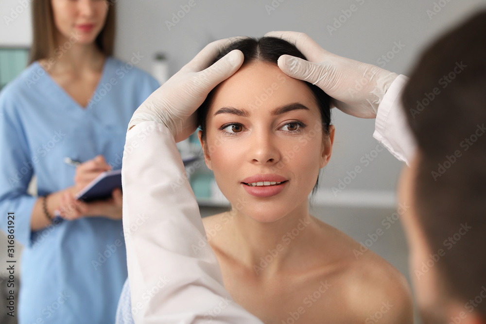 Plastic surgeon examining young womans face prior to operation in clinic