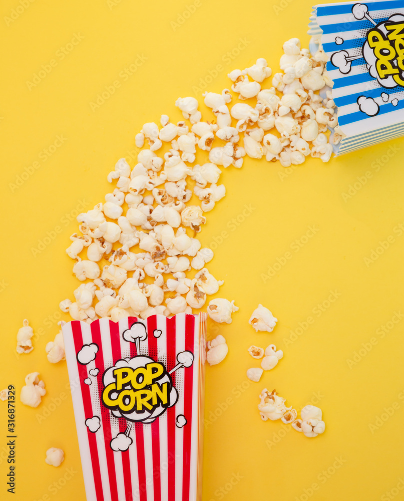 红色爆米花杯中的黄油爆米花，黄色背景下的房子或电影院中的小吃