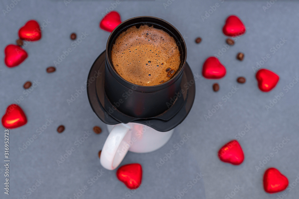 这是在杯子上的滤网里研磨的咖啡，背景是深色的，有谷物和红色的心。