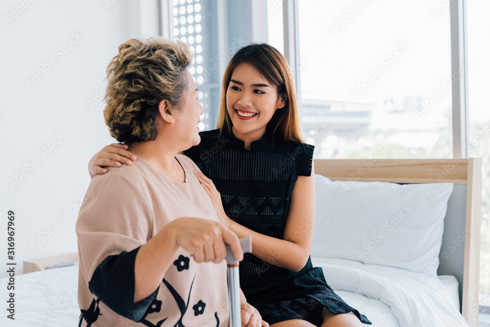 满足于穿着休闲服的年轻亚洲女士在医院病房看望年迈的母亲时面带微笑