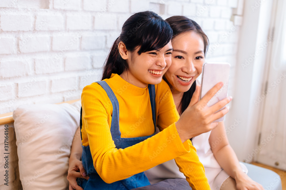 微笑快乐的亚洲十几岁女儿和亚洲中年母亲看着手机的脸