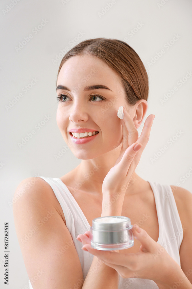Beautiful young woman with jar of cream on light background