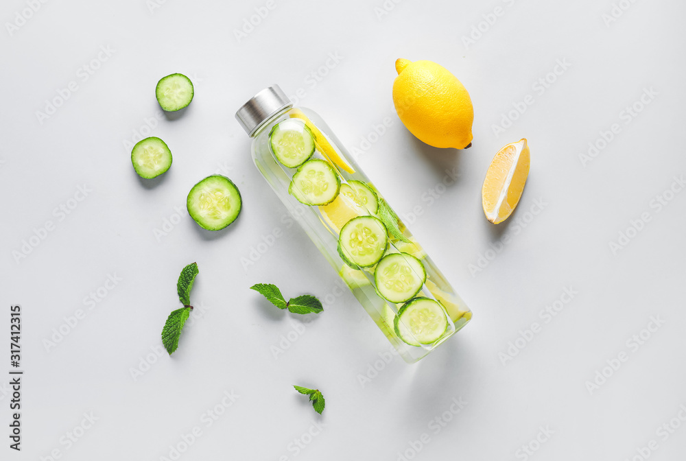 Bottle of cold cucumber water on light background