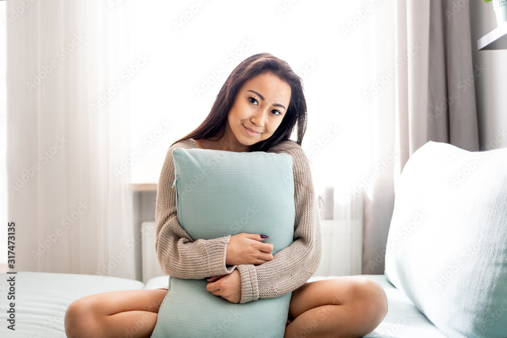 可爱的亚洲年轻女子坐在沙发上，家里有枕头