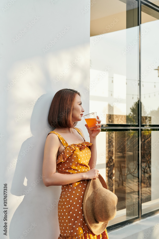 Happy summer woman enjoying orange juice behind the wall