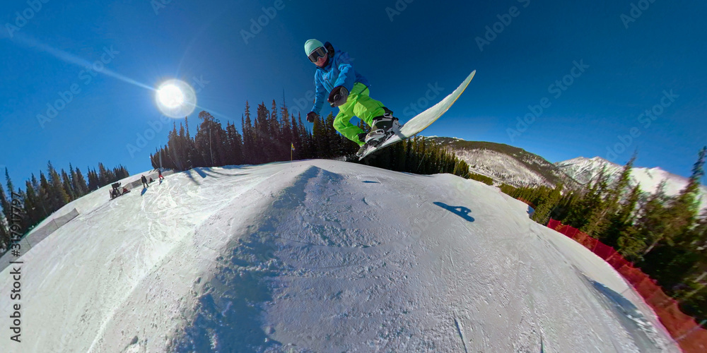 SELFIE：极限单板滑雪运动员在雪地公园里从一名踢球员身上高高跃起。