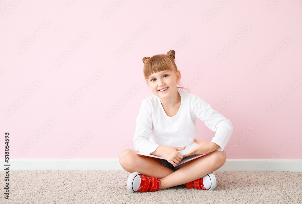 可爱的小女孩拿着书坐在彩色墙上