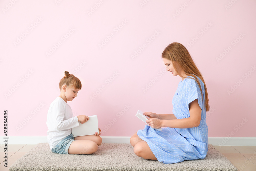 美丽的年轻女子和她的小女儿在彩色墙附近看书