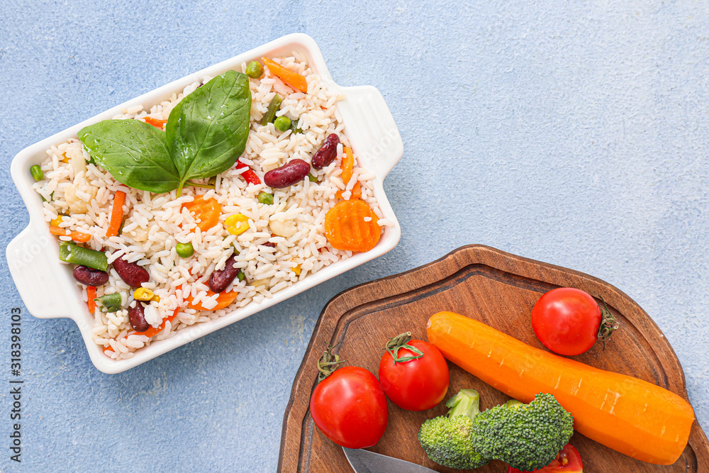 Boiled rice with vegetables in dish on color background