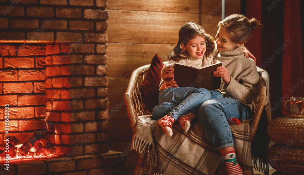 家庭母亲和孩子在冬天的晚上在壁炉旁看书喝茶。