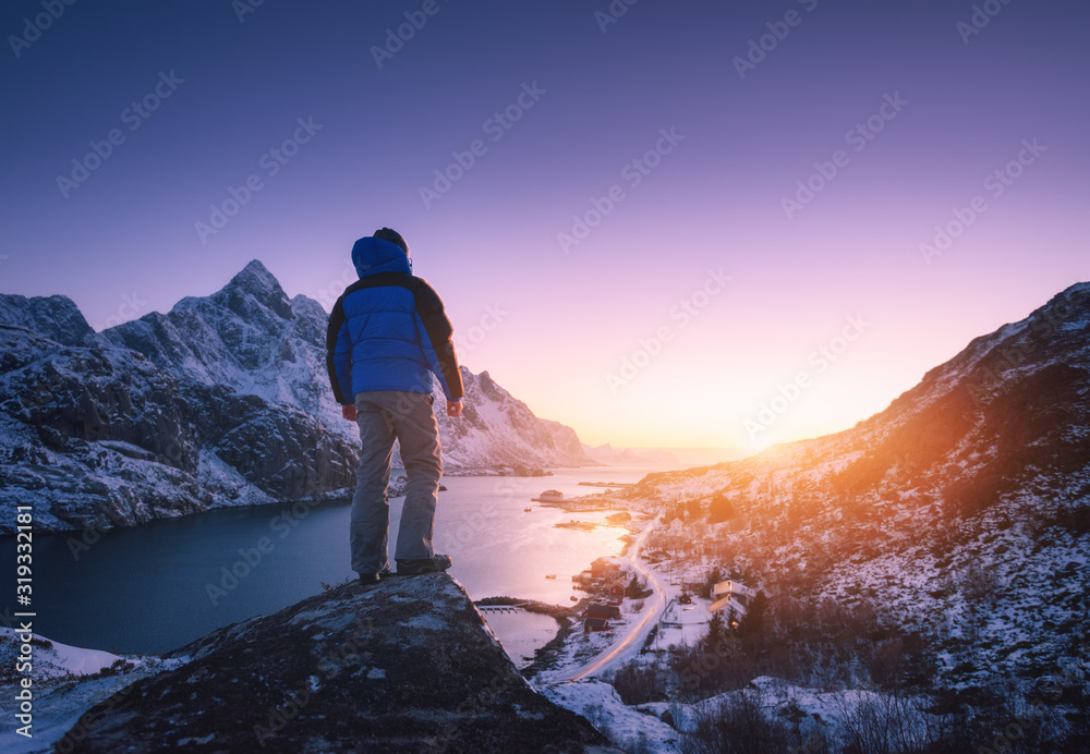 冬天，在五彩缤纷的日落下，人类站在雪山和峡湾的山峰上。哟