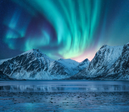 北极光笼罩在雪山、湖岸和水中的倒影。北极光