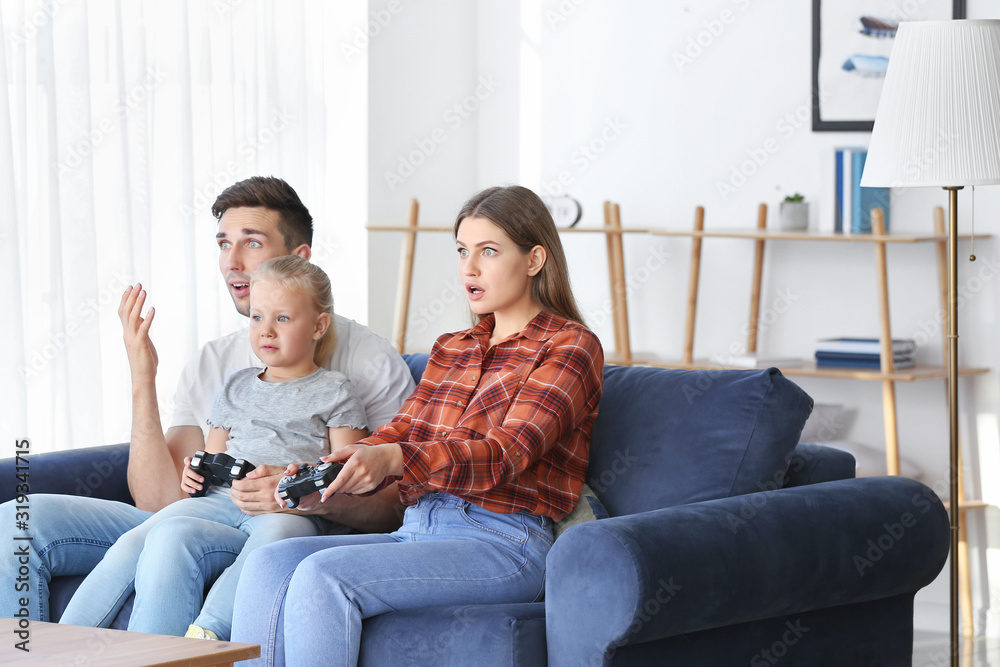 年轻的一家人坐在家里的沙发上玩电子游戏