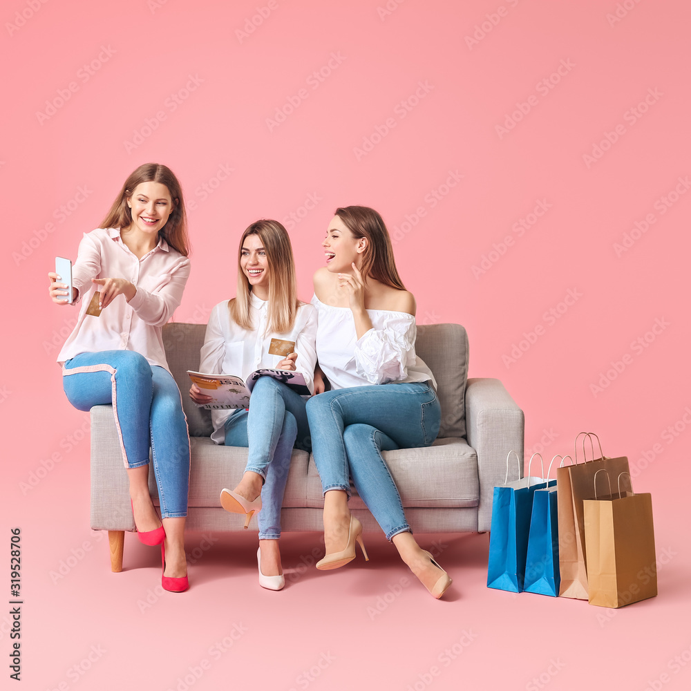 背着彩色背景，拿着购物袋、信用卡和手机坐在沙发上的年轻女性