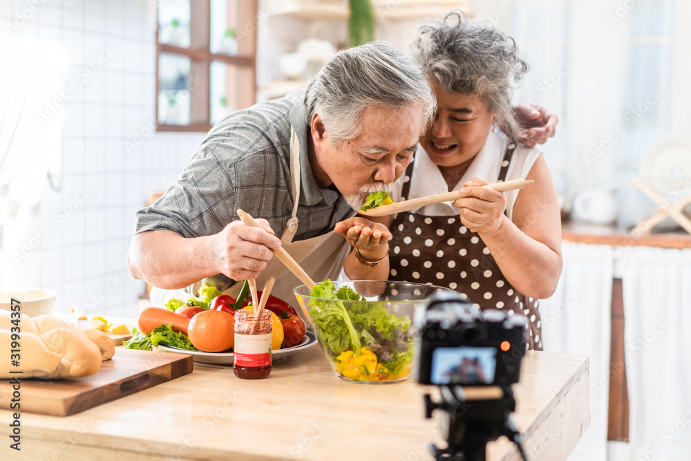 一对年长的亚洲老人幸福地住在家里的厨房里。爷爷在做饭后吃沙拉