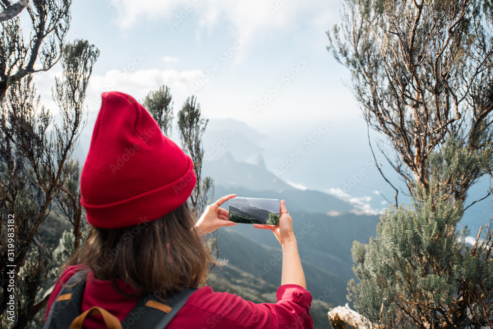戴红帽子的女人在特内里费岛岩石海岸线用手机拍摄令人惊叹的景色