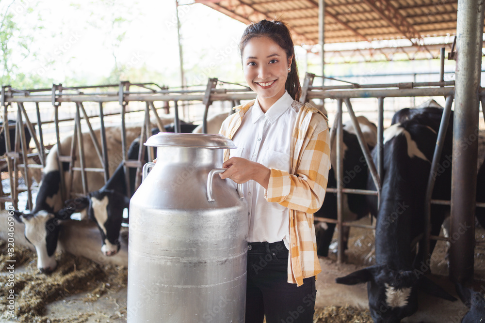 一个亚洲女人拿着一个装牛奶的容器在他的农场里。