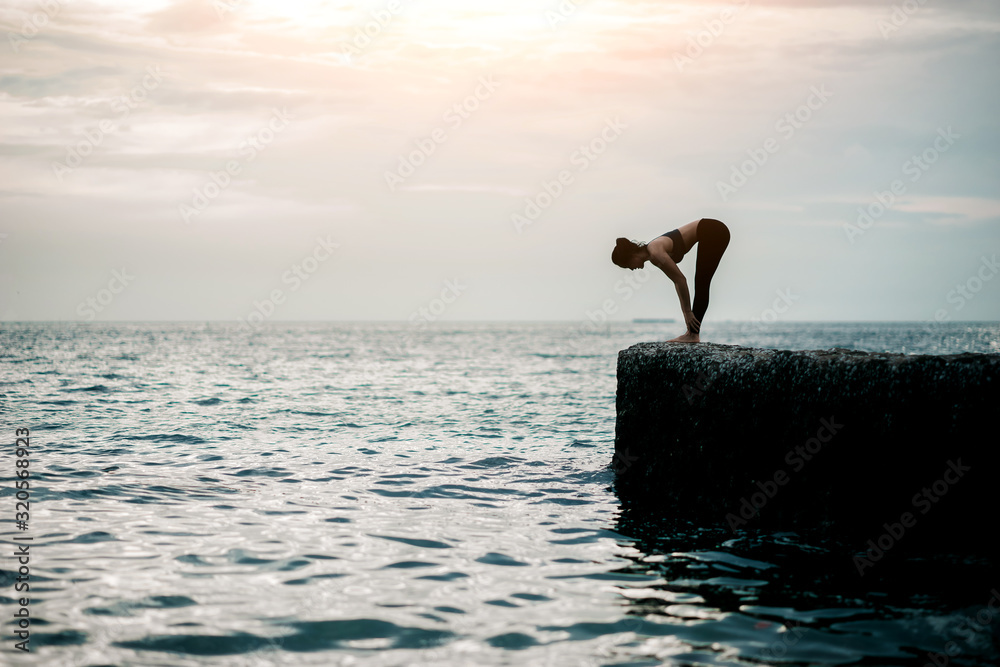 Young Asian woman practicing yoga exercise at quiet rock pier with sea background. Sport and recreat