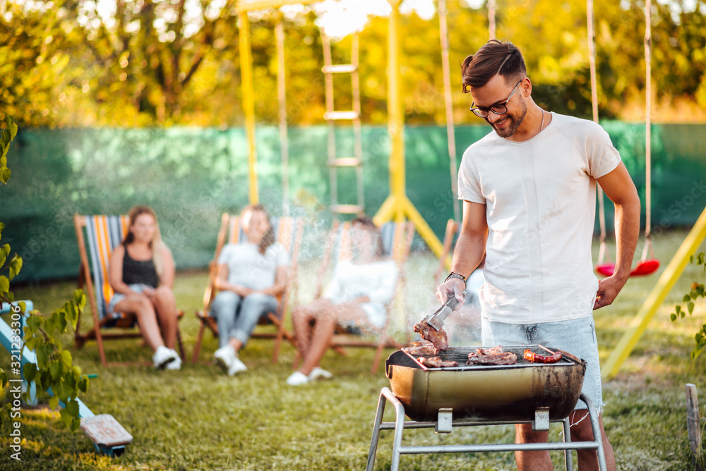 Summertime fun. Portrait of a young man grilling meat on the barbecue grill outdoors.