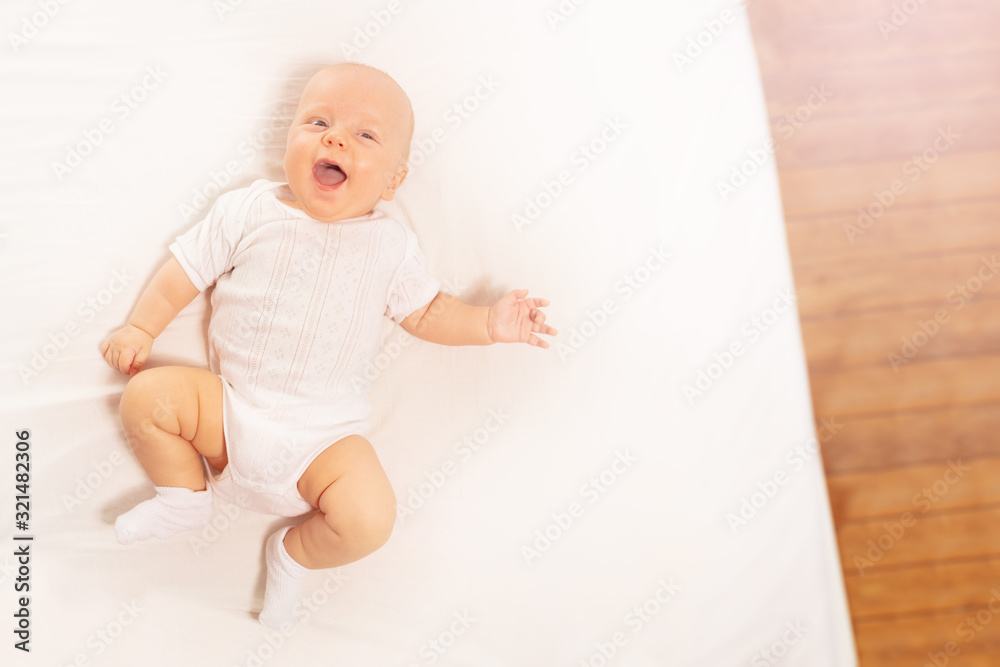 Laughing happy little infant baby boy with open mouth moving hands and legs view from above