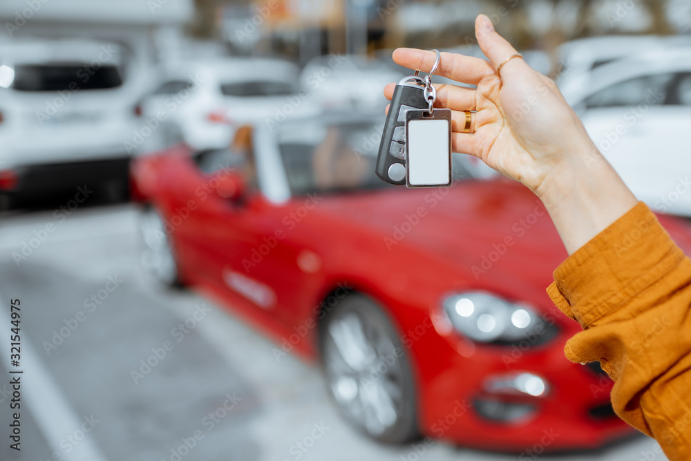 一名女子在户外停车场拿着一辆新购买或租赁的红色汽车的钥匙扣，特写