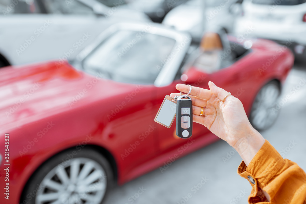 在户外停车场，一名女子拿着一辆新购买或租赁的红色汽车的钥匙扣，特写